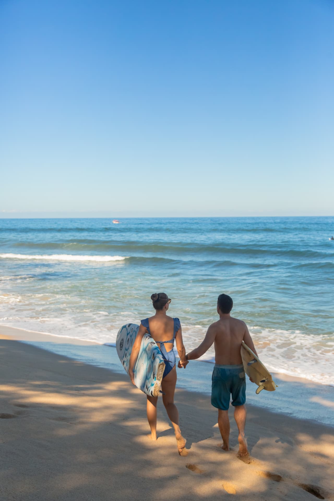 Pareja caminando hacia el mar con tablas de surf