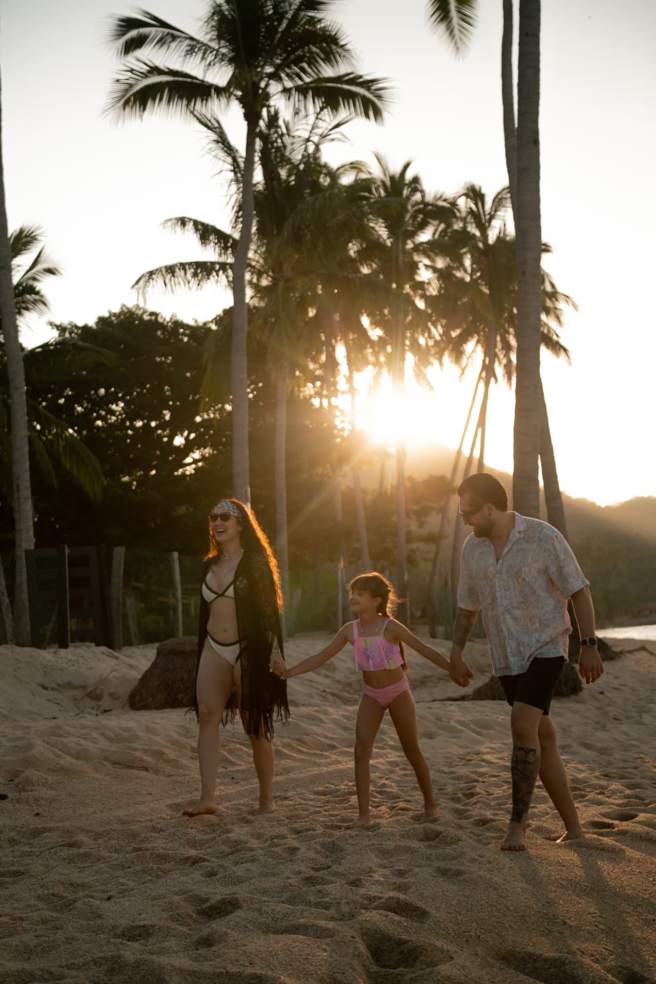 Parents and their daughter walking the beach at sunset among the palms