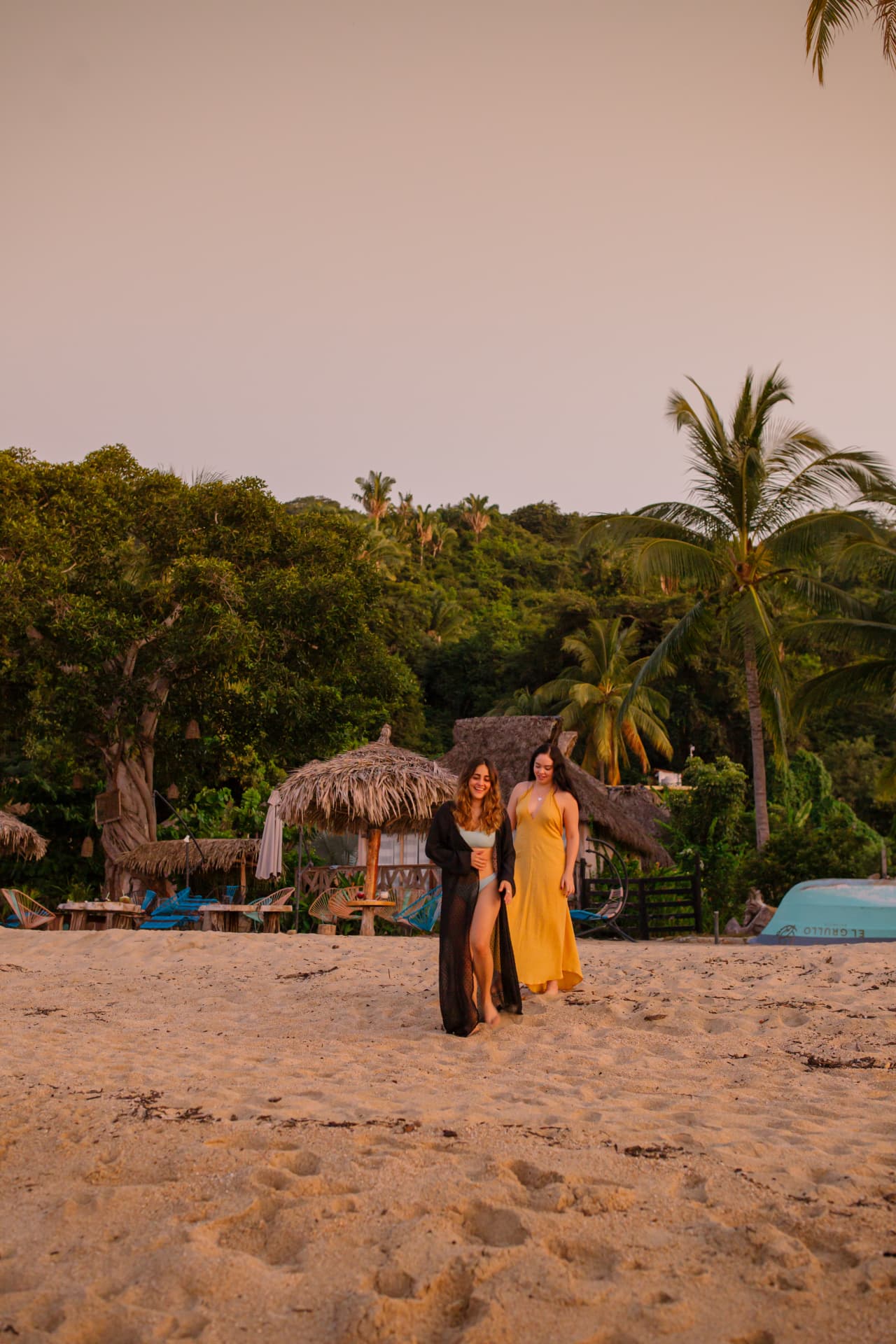 Two friends walking on the sand in front of the hotel at sunset