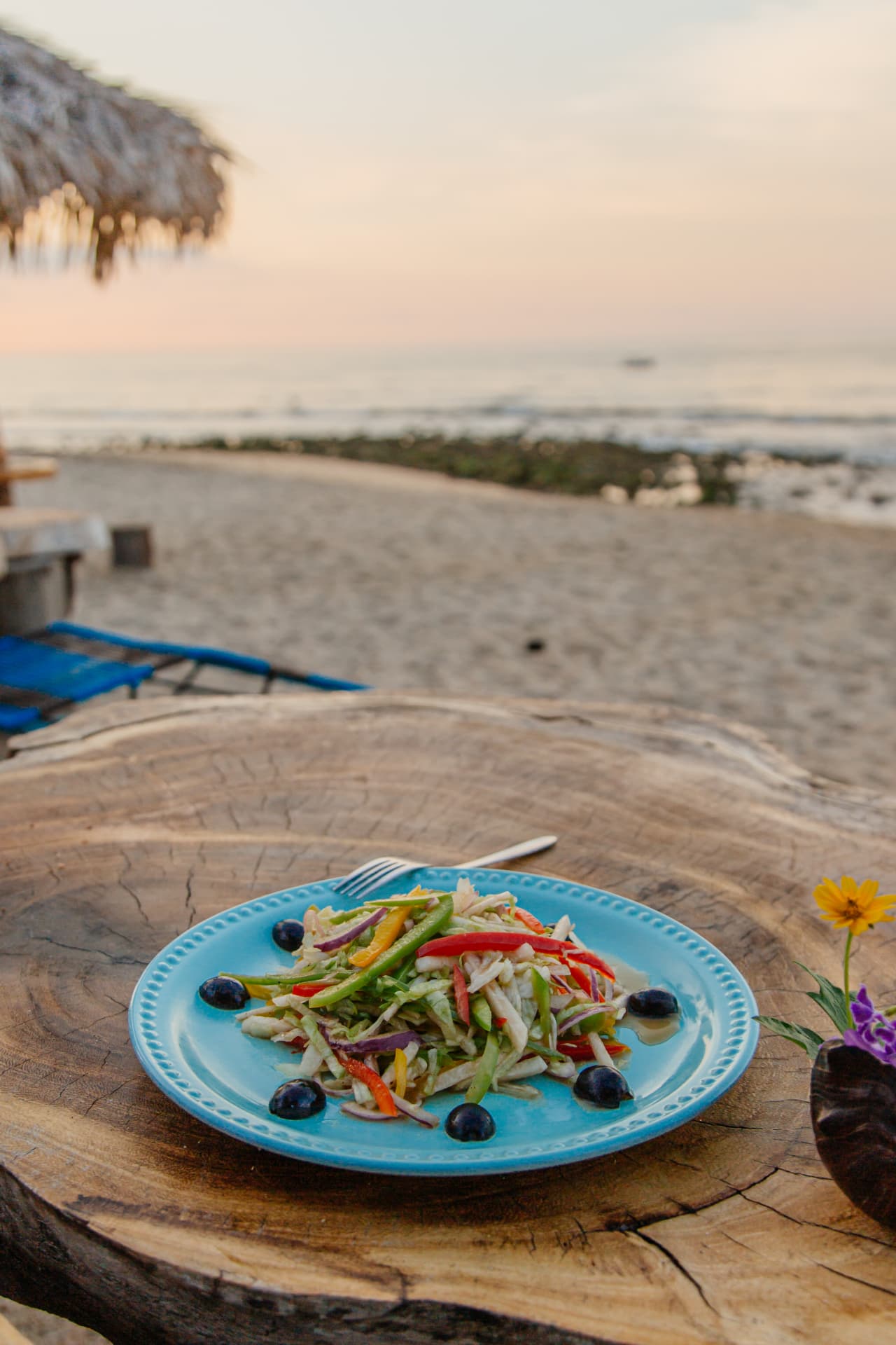 Ensalada fresca en plato turquesa frente al mar al atardecer