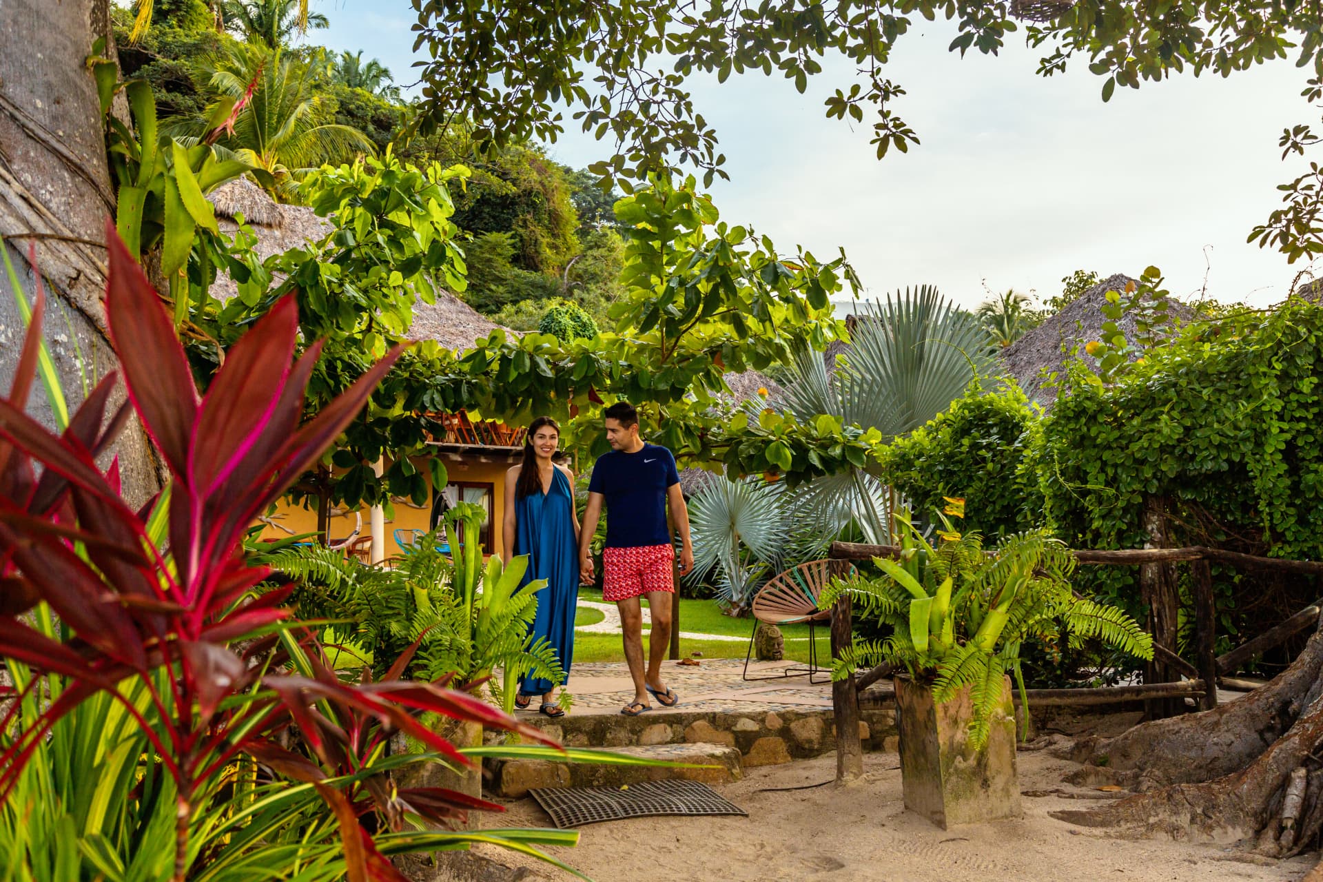 Pareja caminando de la mano por el jardín tropical del hotel
