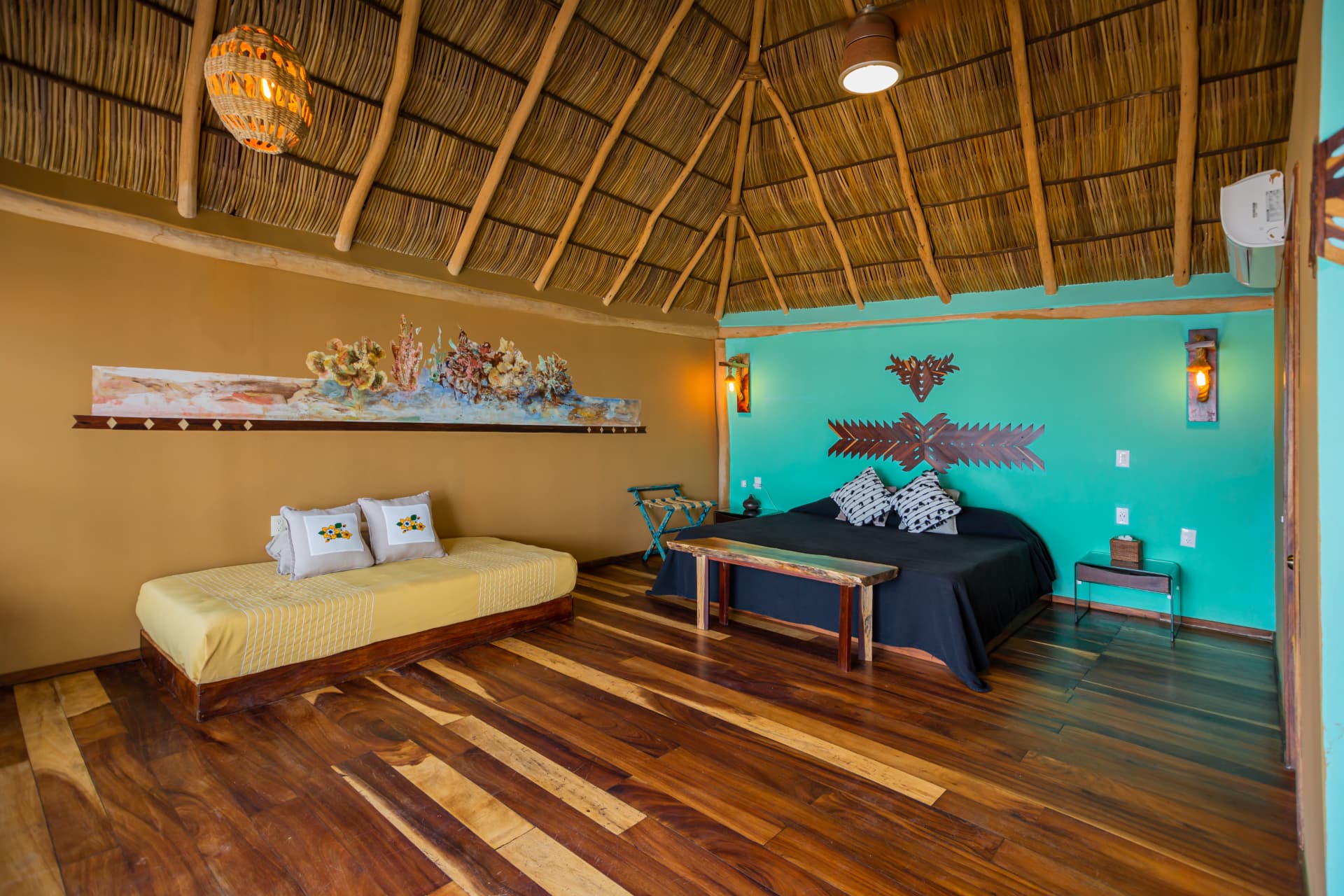 Interior de la suite con techo de palapa alto y muro turquesa