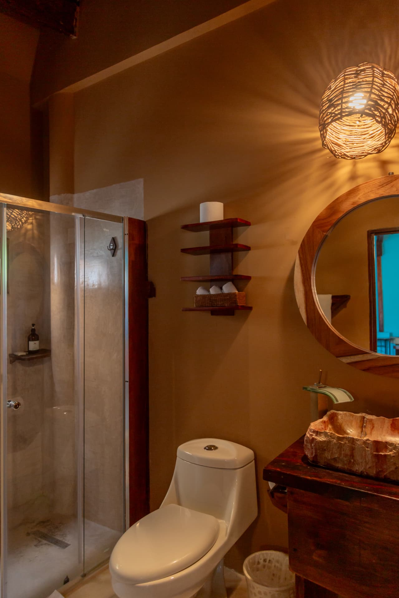 Montaña: baño con regadera de cristal, lavabo de piedra y espejo redondo de parota