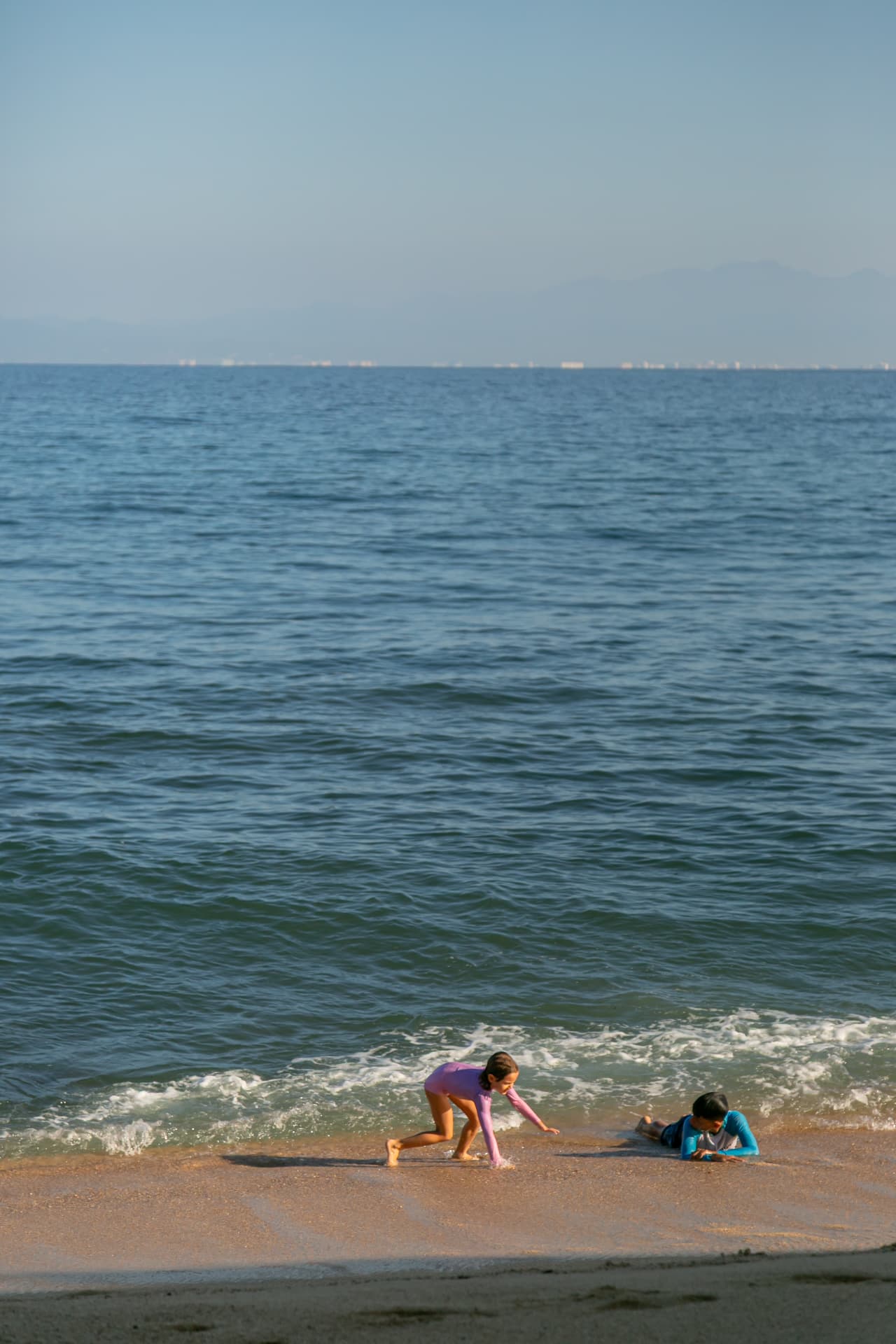 Two children playing in the waves at the shore of Quimixto beach