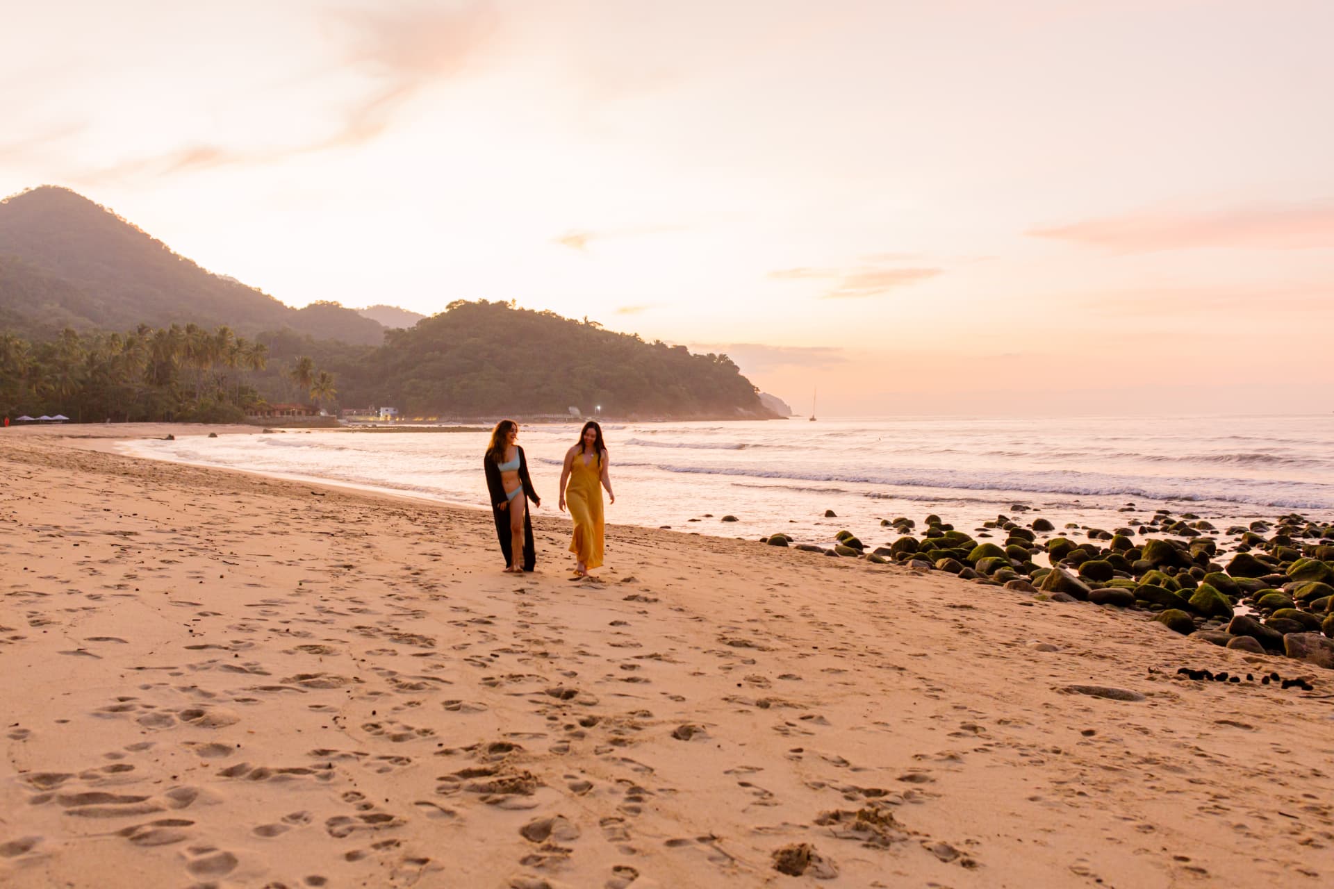Two friends walking the shoreline with the mountains behind at sunset