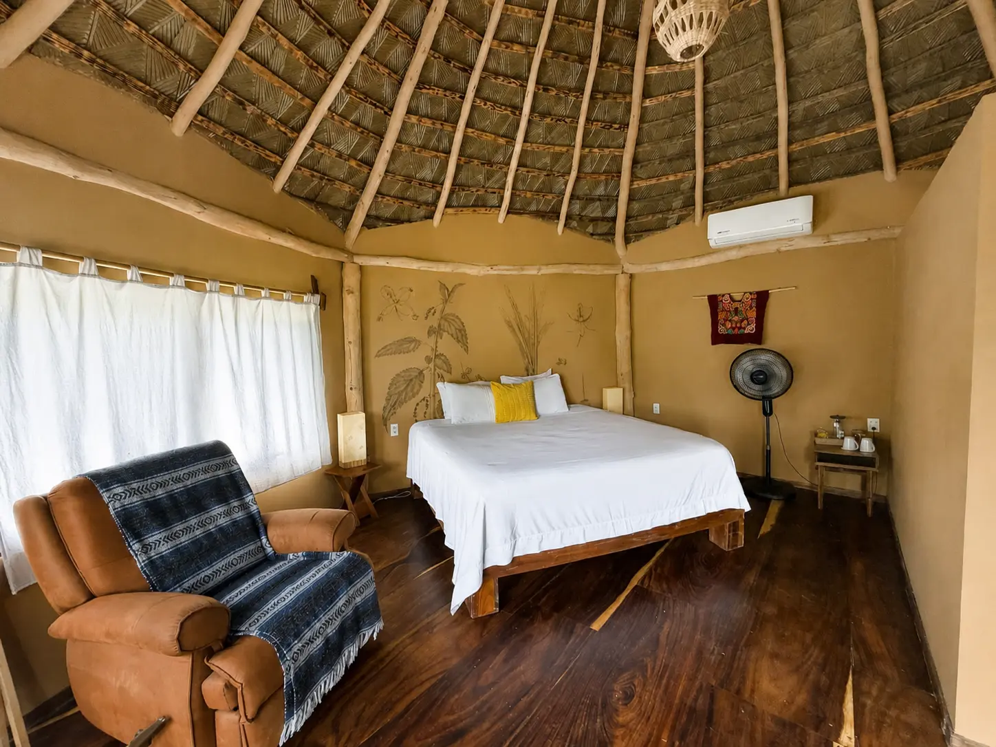 Interior con cama King, murales botánicos y techo de palapa alto