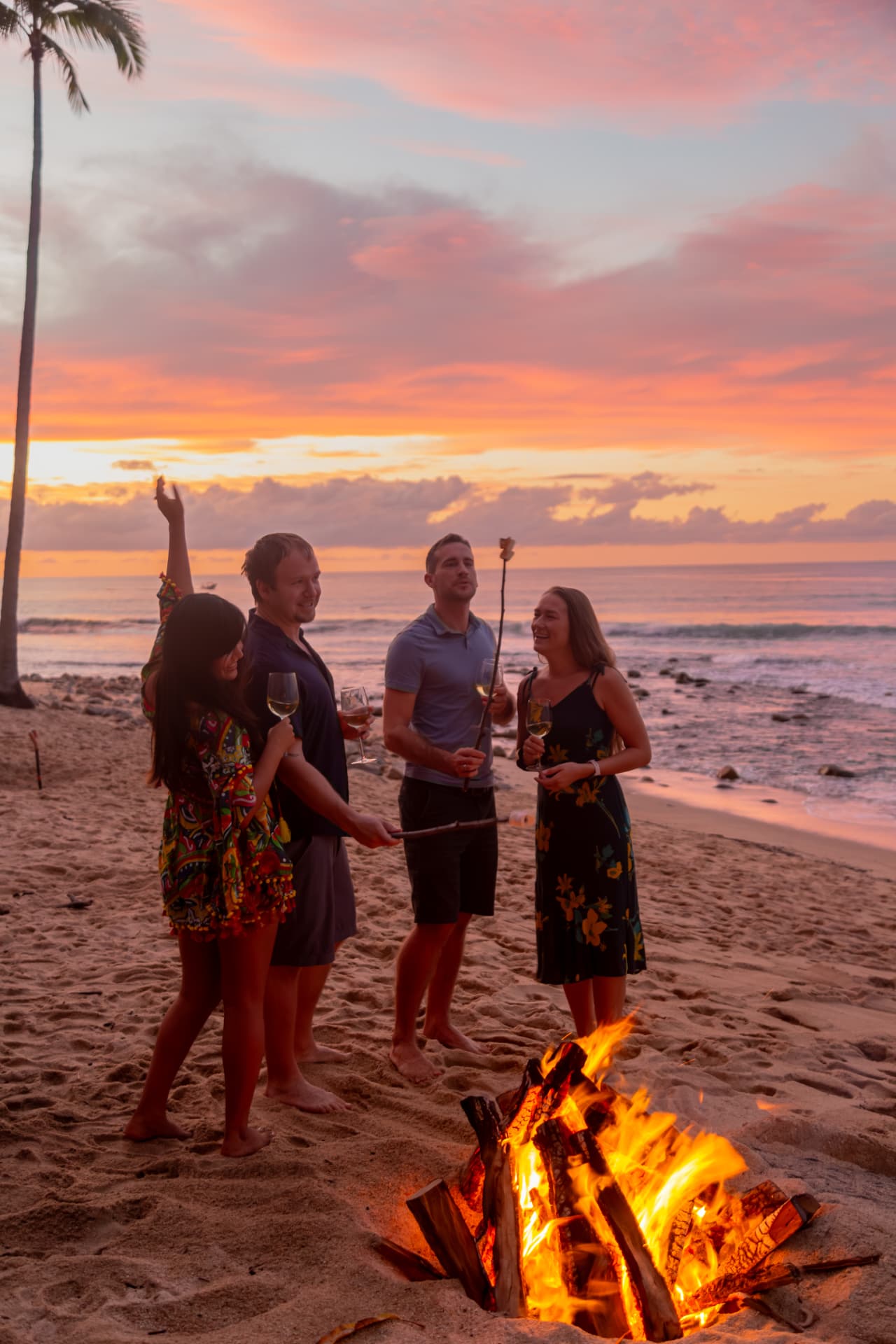 Grupo de amigos alrededor de una fogata en la playa al atardecer