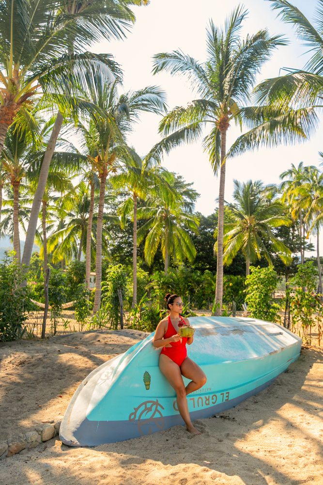 Viajera sola con un coco frente a una panga entre palmeras