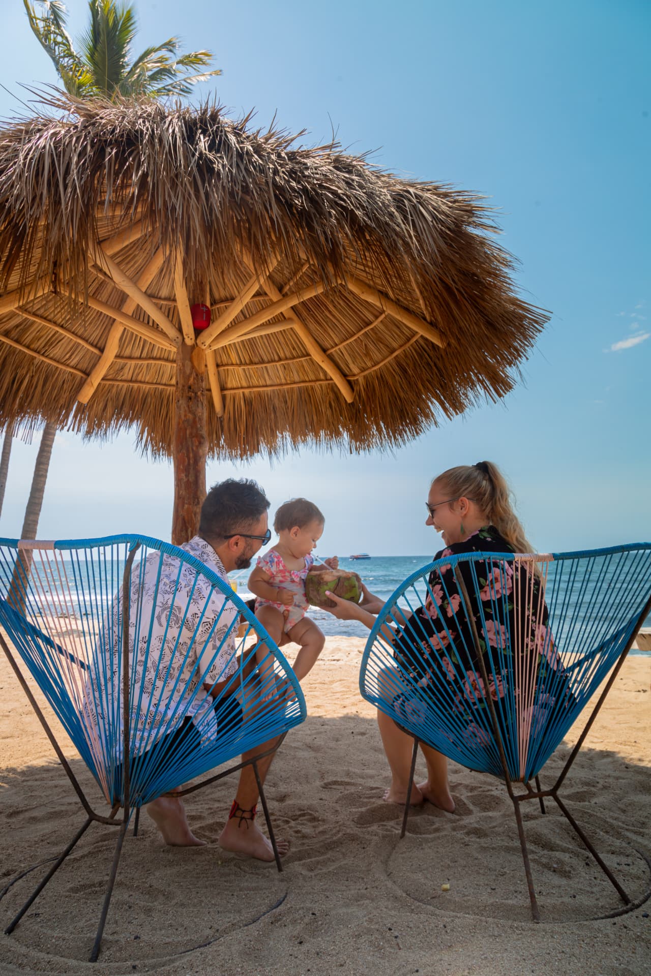 Family by the sea sharing a coconut under the palm umbrella