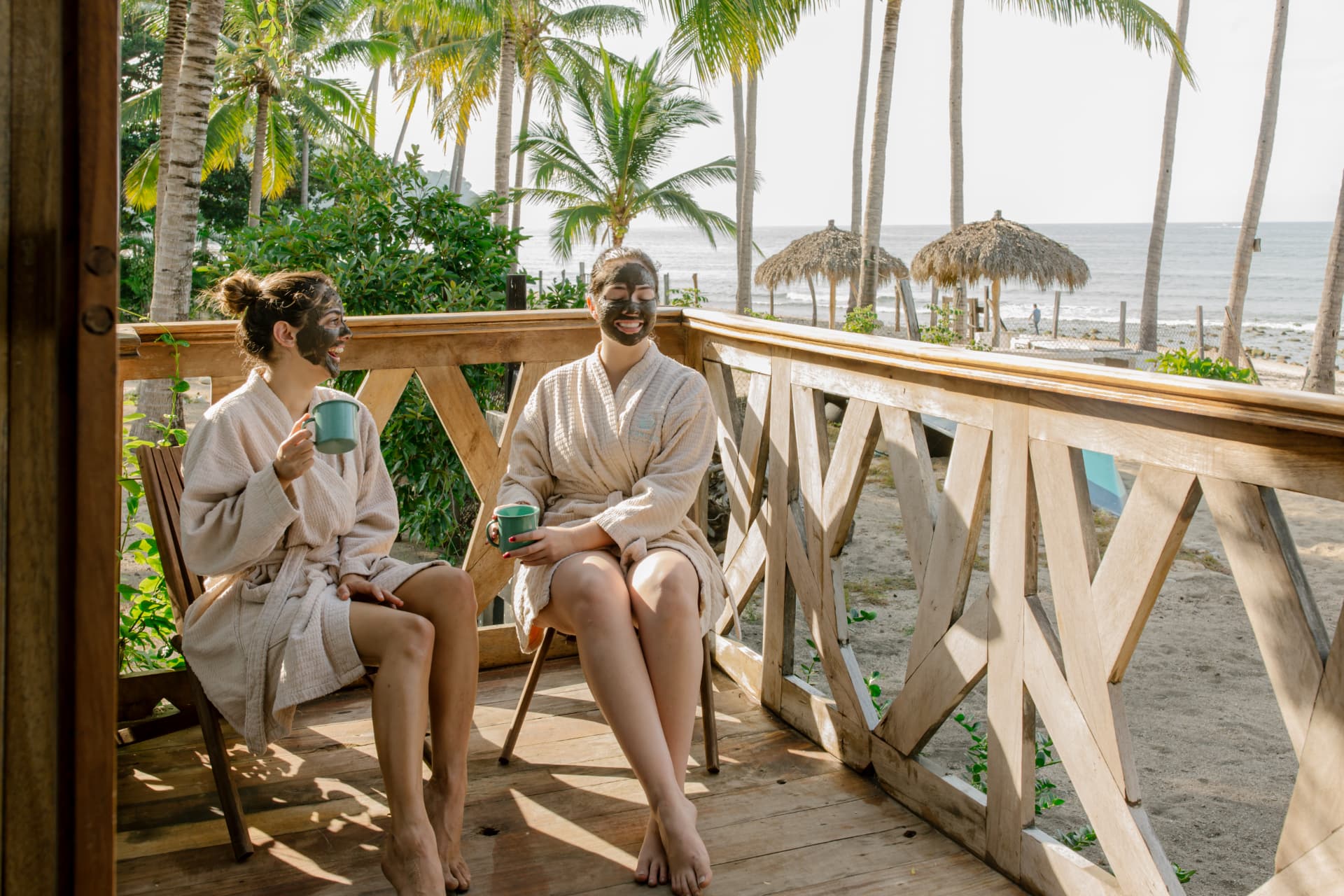 Two guests in clay masks having tea on the oceanfront deck