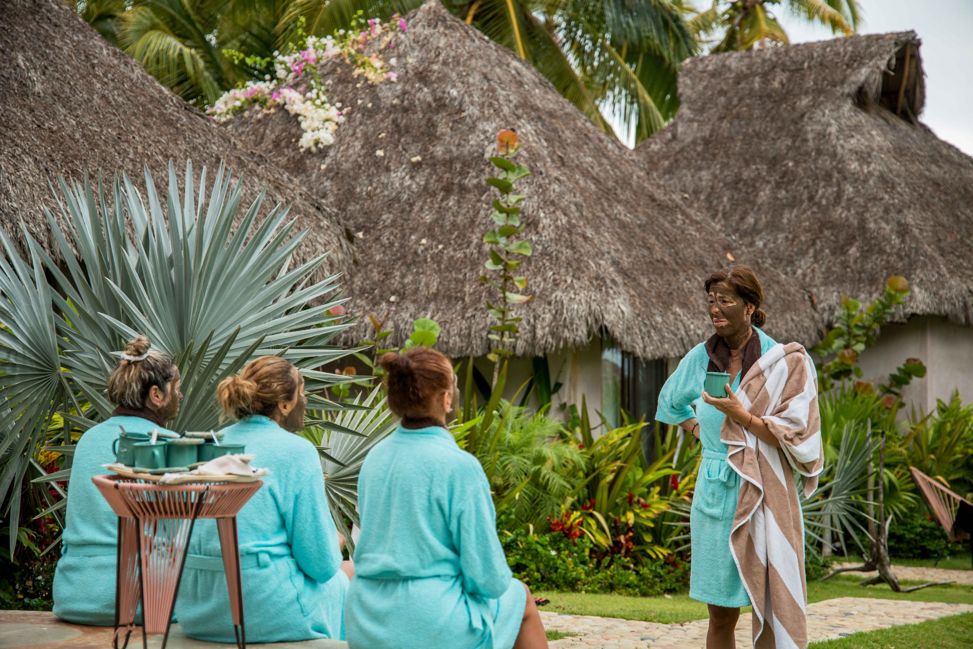 Group in robes with clay masks among the palapas