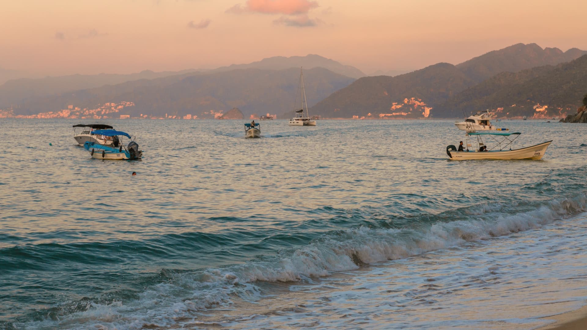 Pangas and a catamaran off the beach with the bay mountains at sunset
