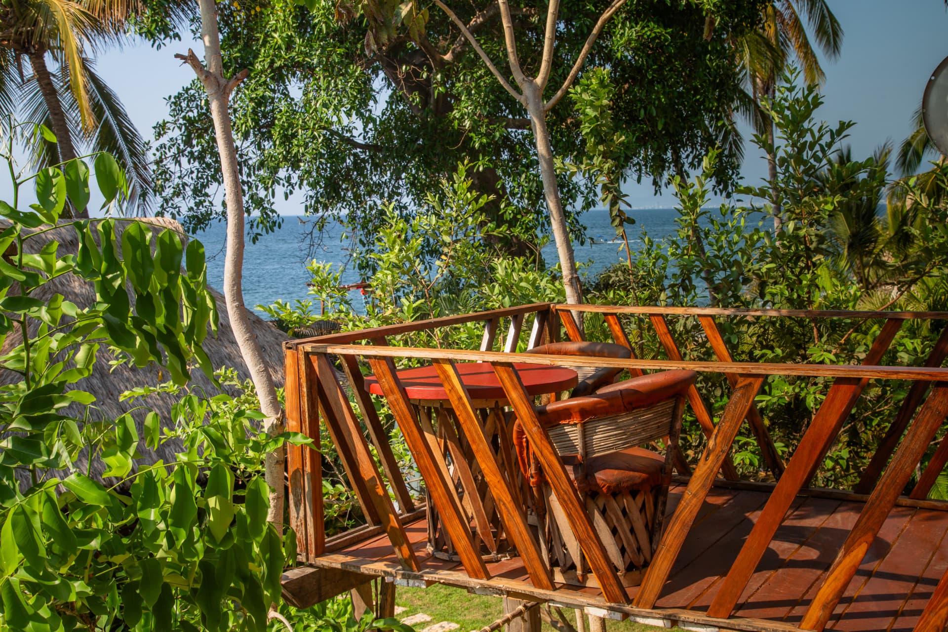 Wooden terrace with table and chairs and an ocean view through the jungle