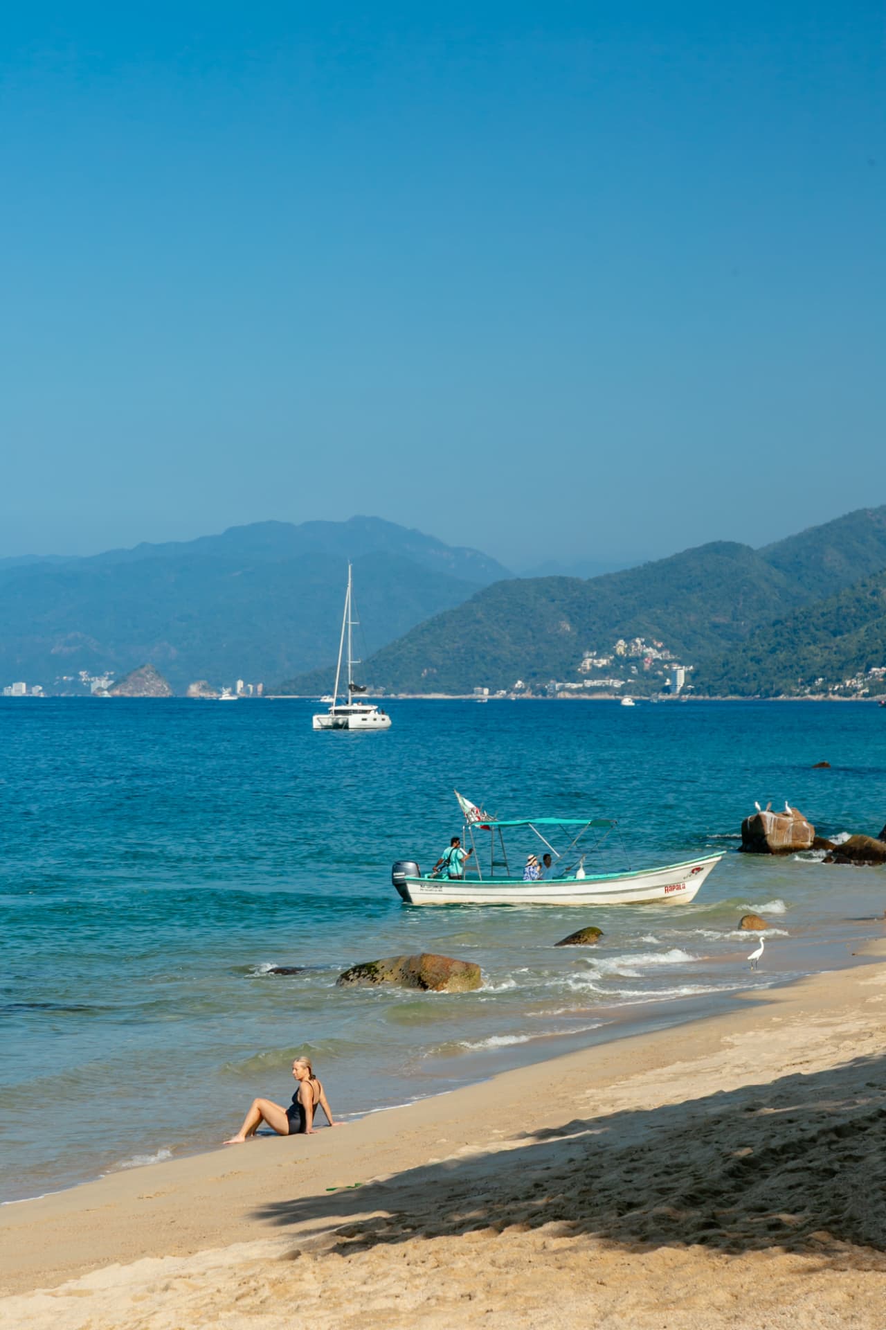 Guest sitting on the shore as a boat pulls up to Quimixto beach