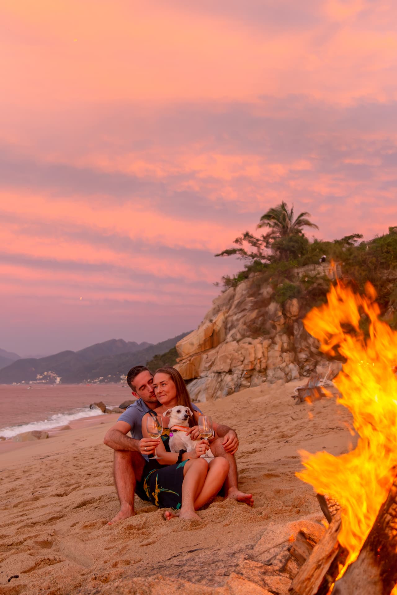 Couple with their dog beside the bonfire under a pink sky