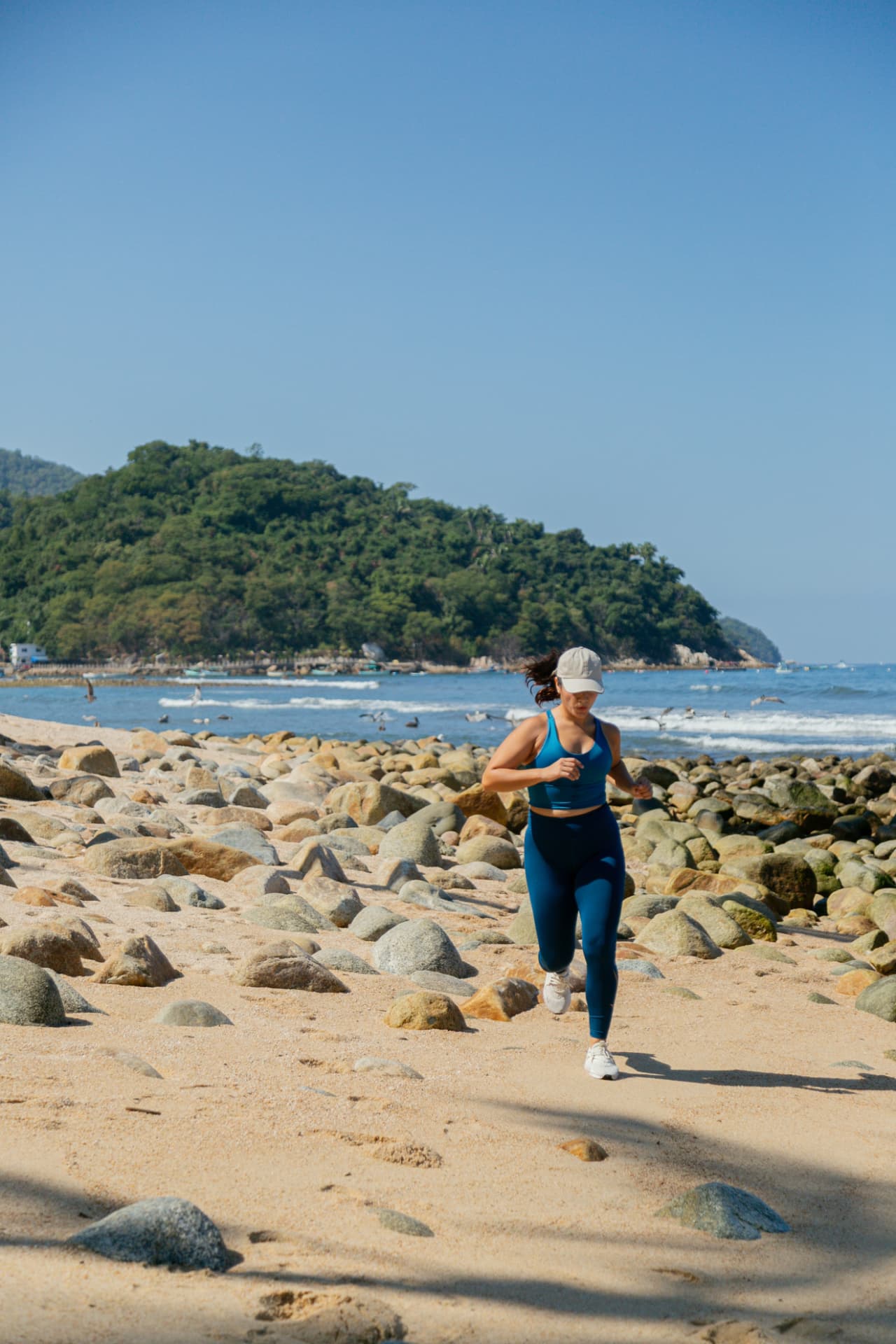 Woman running along Quimixto beach with the green hills behind